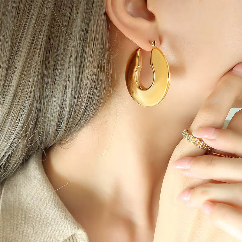 Gold hoop earrings worn by a person with a neutral background