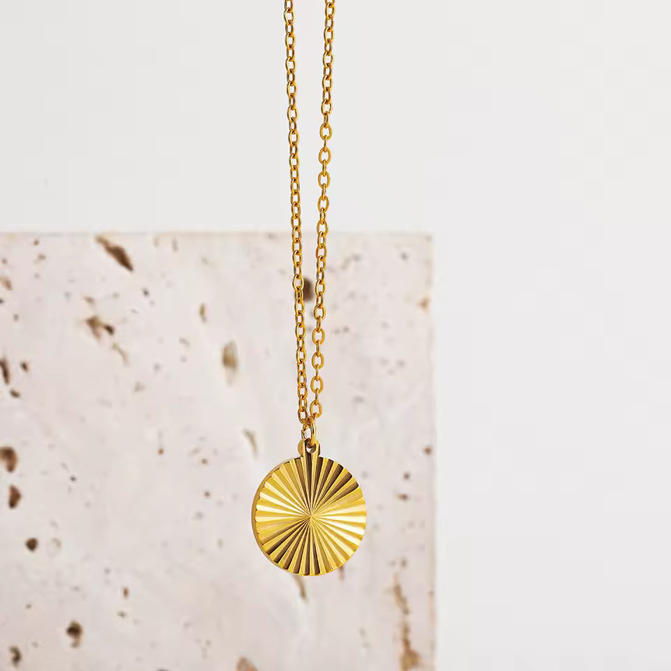 Gold necklace with a sunburst pendant on a light background